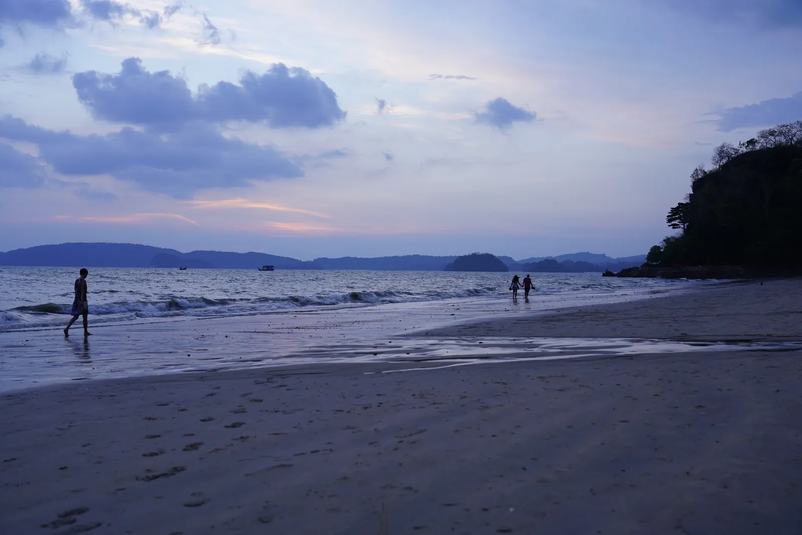Ao Nang beach at dusk with calm water, a few people on the sand and a headland on the right