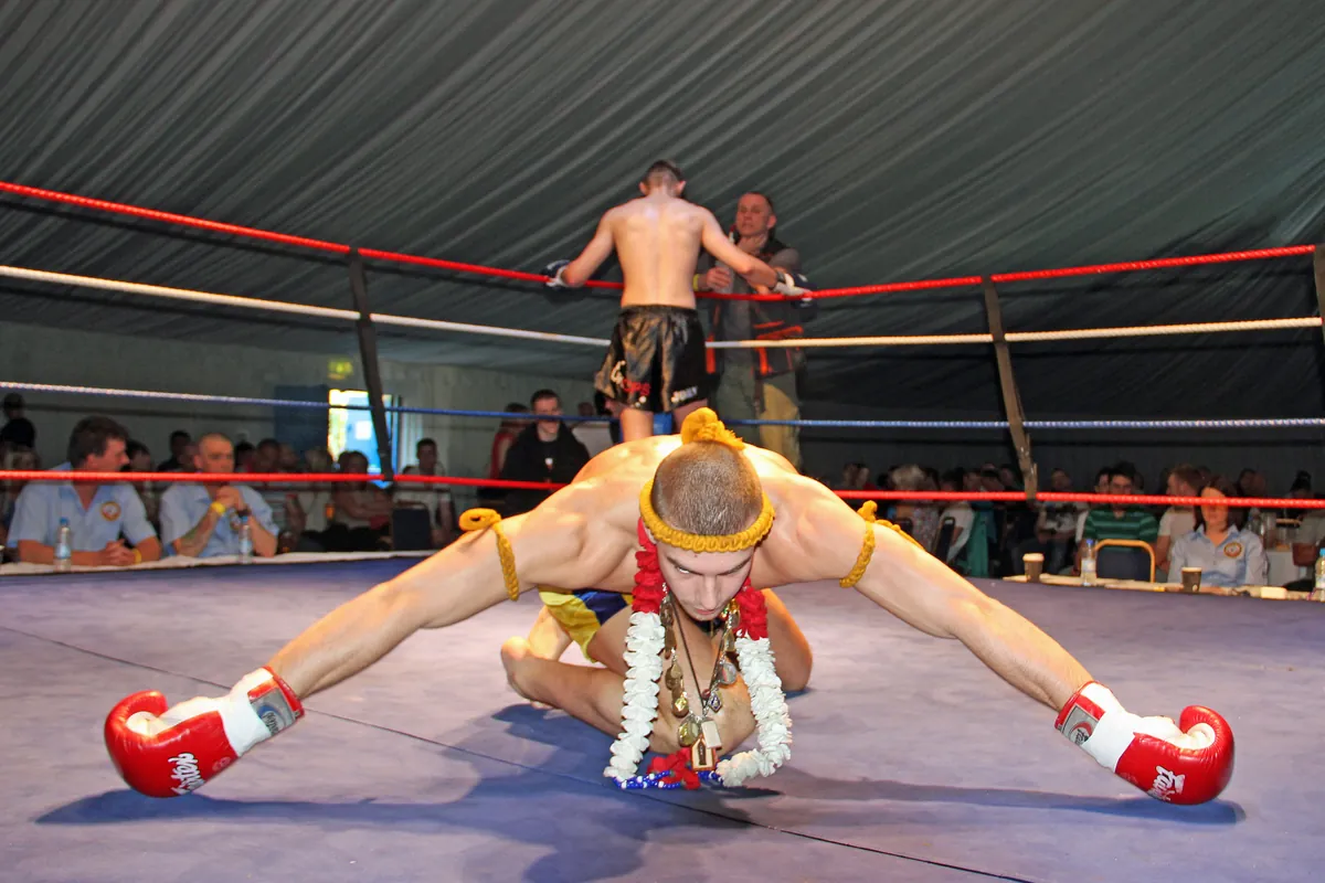 A Muay Thai fighter in a gold headband and armbands bowing low in the ring during the Wai Khru Ram Muay